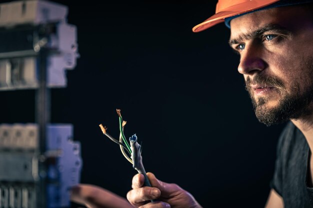 A male electrician works in a switchboard with an electrical connecting cable