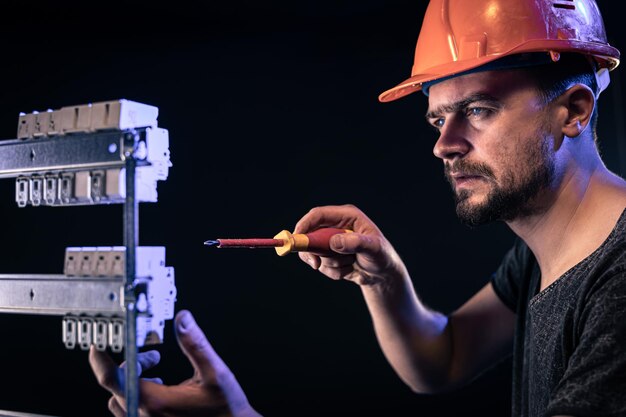 A male electrician works in a switchboard with an electrical connecting cable