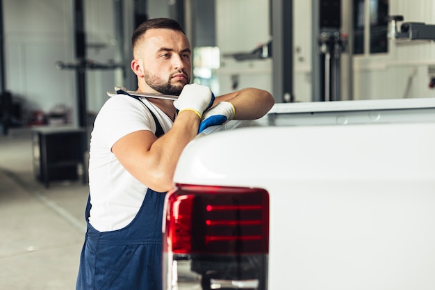 Free photo male employee leaning on car and holding wrench