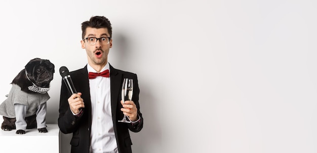 Male entertainer raising glass of champagne giving microphone to cute black dog standing over white