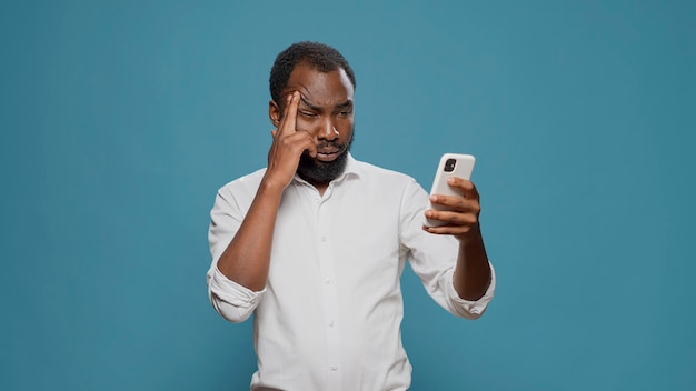 남성 기업가는 두통을 없애기 위해 관자놀이를 문지르고 스마트폰을 사용하여 문자 메시지를 보냅니다. 편두통으로 고통받고 불행한 젊은 남자가 휴대전화로 일하고 있습니다.