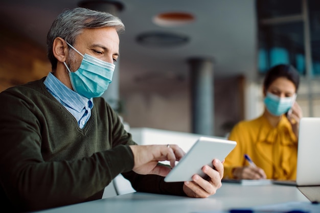 Male entrepreneur with face mask using digital tablet while working in the office