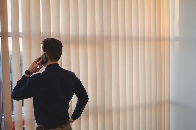 Male executive talking on mobile phone near window blinds