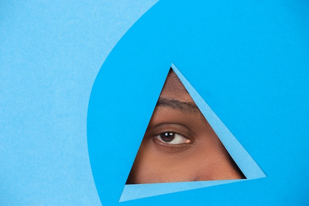 Male eye looking, peeking throught triangle in blue background