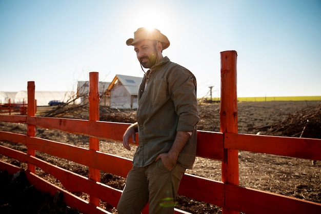 Foto gratuita agricoltore maschio in posa accanto al recinto della fattoria