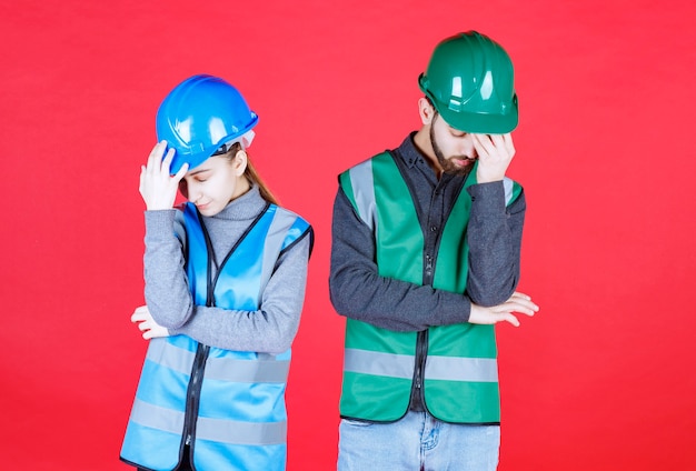 Male and female engineers wearing helmet and gear look tired and sleepy.