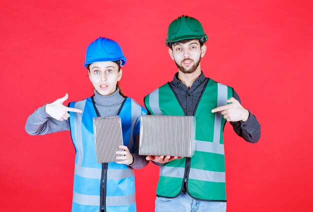 Male and female engineers with helmets holding silver gift boxes.