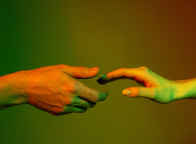 Male and female hands reaching each other, studio shot on red green background in neon lights
