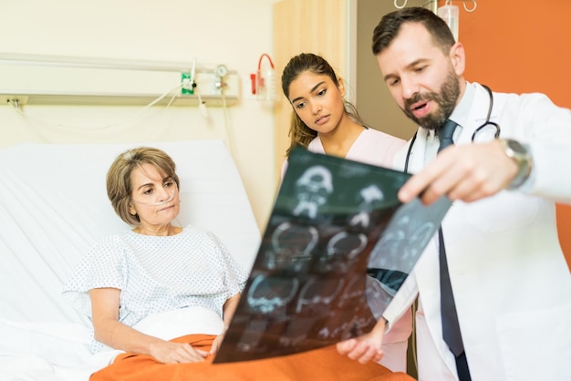 Male and female healthcare workers explaining xray diagnosis to senior patient suffering breathing problems in hospital