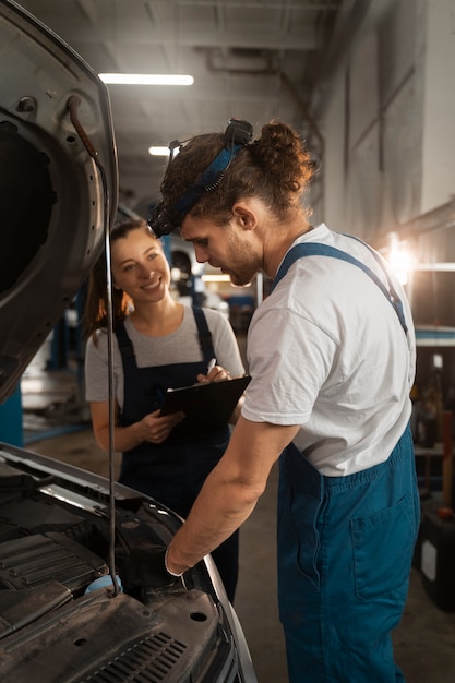 Foto gratuita meccanici maschili e femminili che lavorano nel negozio su un'auto