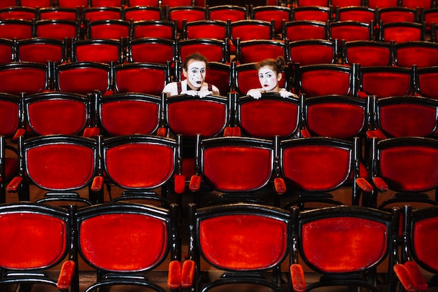 Free photo male and female mime artist hiding behind the row of arm chairs