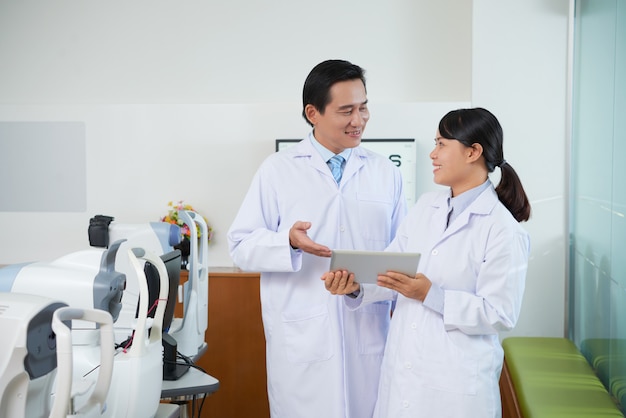 Male and female ophtalmologists discussing something on tablet in eye examination room