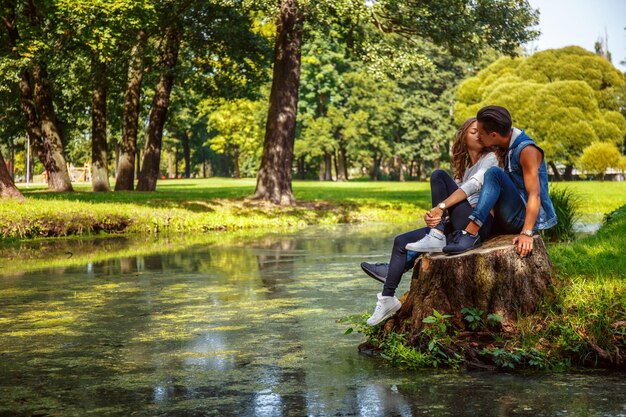 Male and female relaxing and kissing near river in a park.