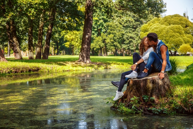 Мужчина и женщина расслабляются и целуются у реки в парке.