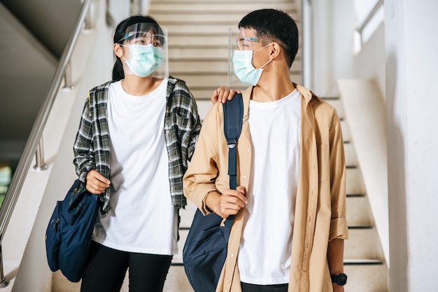 Male and female students wear a health mask and talk to each other on the stairs.