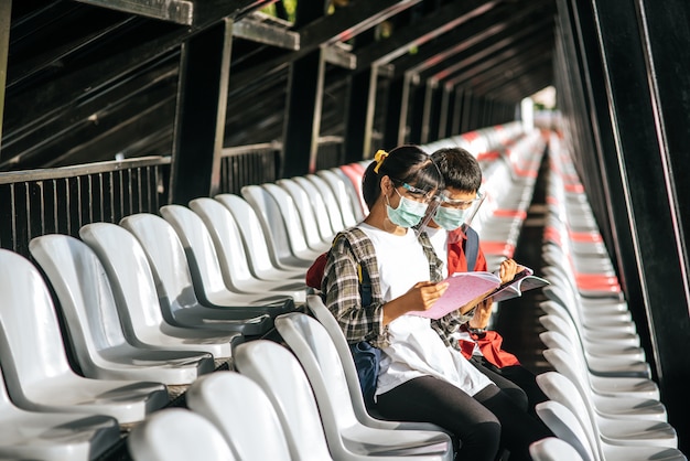 Male and female students wear masks and sit and read on the field chair