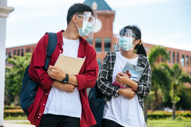 남녀 학생은 마스크를 쓰고 대학 앞에 서 있습니다.