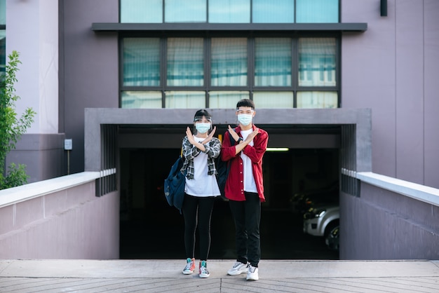 Male and female students wear masks and stand in front of the university.