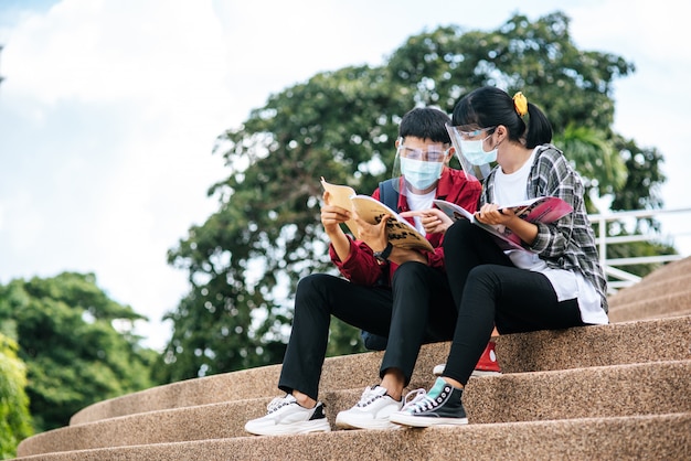 Free photo male and female students wearing masks sit and read books on the stairs