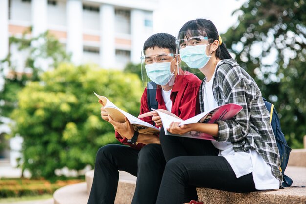 マスクをした男性と女性の学生が座って階段で本を読む