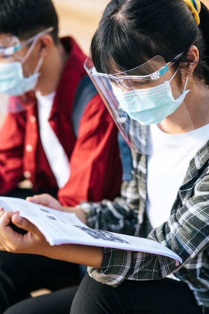 Free photo male and female students wearing masks sit and read books on the stairs