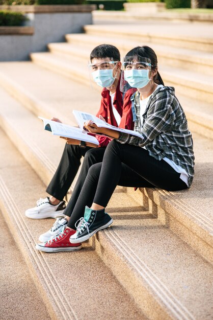 마스크를 착용하는 남녀 학생이 앉아서 계단에서 책을 읽습니다.