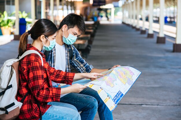 Male and female tourists look at the map beside the railway.