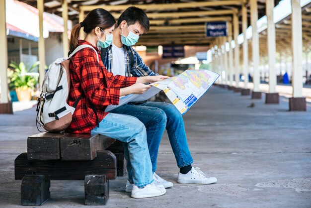 Male and female tourists look at the map beside the railway.