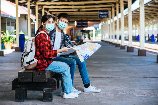 Туристы мужского и женского пола смотрят на карту возле железной дороги.