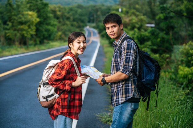 Male and female tourists look at the map on the road.