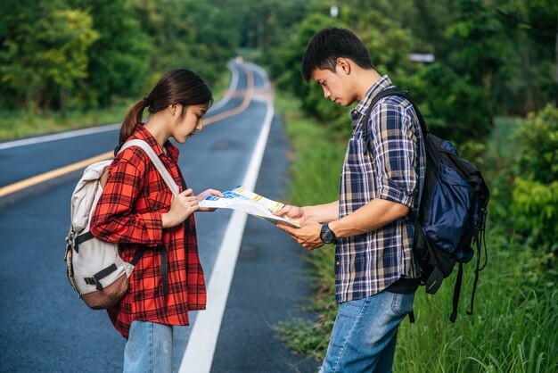 Male and female tourists look at the map on the road.