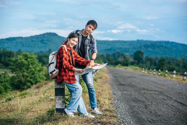 立っている男性と女性の観光客が道端の地図を見てください。