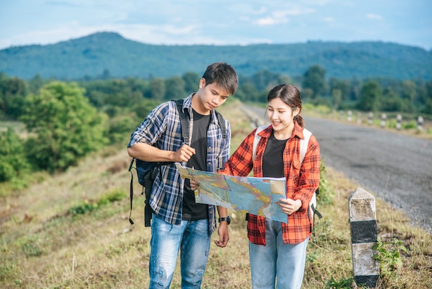 Free photo male and female tourists standing look at the roadside map.