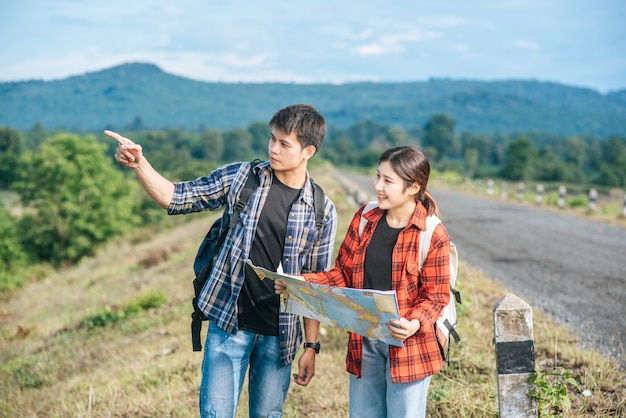 立っている男性と女性の観光客が道端の地図を見てください。