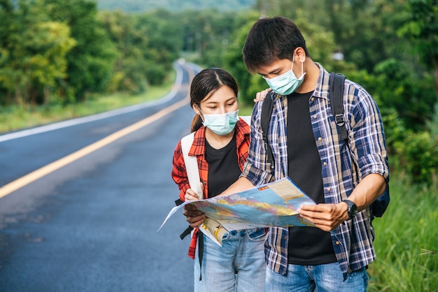 Male and female tourists wear medical masks and look at the map on the street.