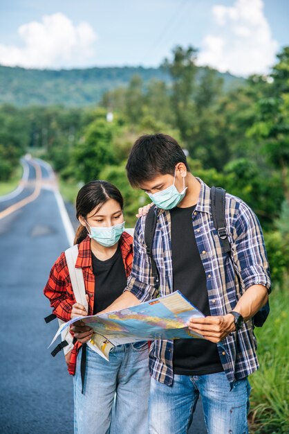 남성과 여성 관광객은 의료 마스크를 쓰고 거리의지도를 봅니다.