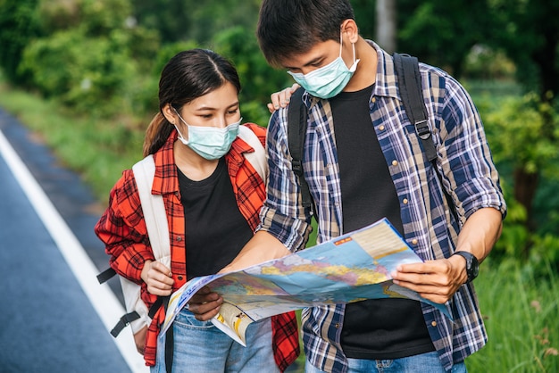 Male and female tourists wear medical masks and look at the map on the street.