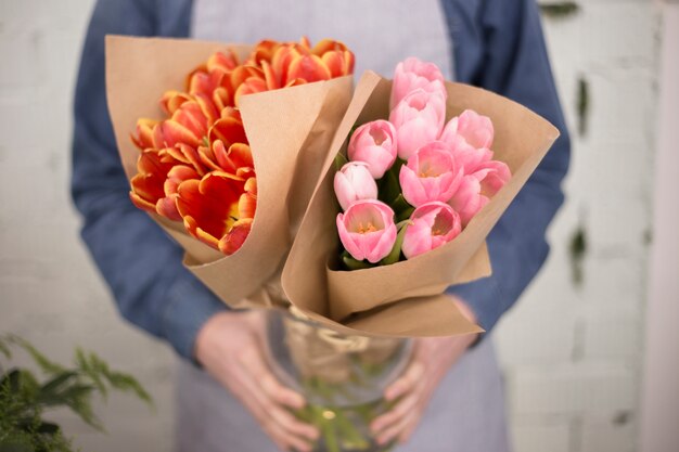 Мужской флорист держит букет розовых и оранжевых тюльпанов, завернутый в бумагу