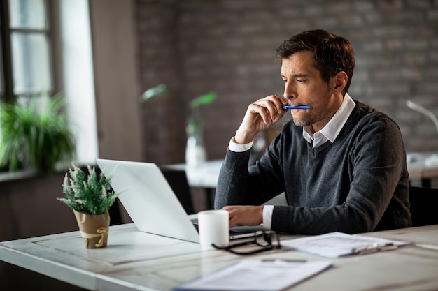 Male freelance worker reading an email while working on laptop in the office