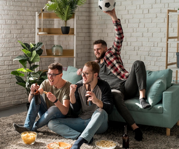 Male friends watching sports on tv and drinking beer with snacks