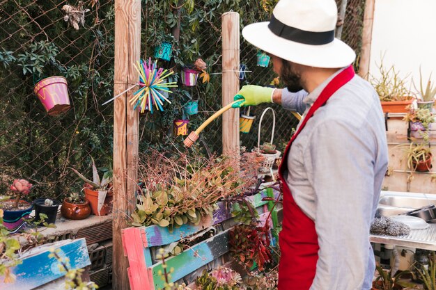 Male gardener wearing hat watering the plant in garden with hose