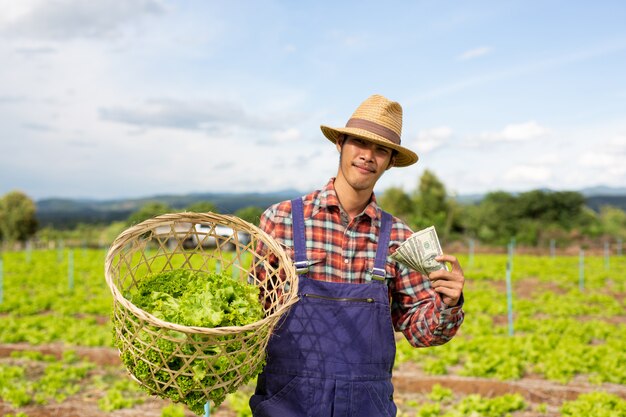 Male gardeners who hold vegetables and dollar currency in their hands.