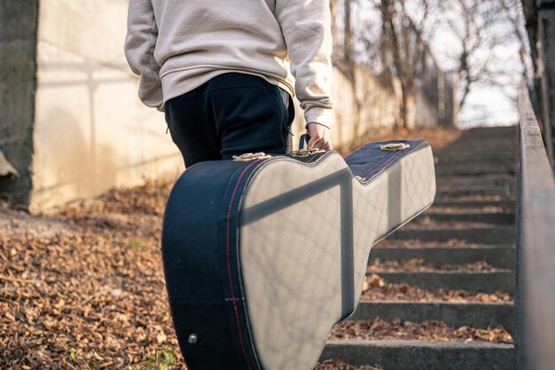 A male guitarist carries a guitar case outside