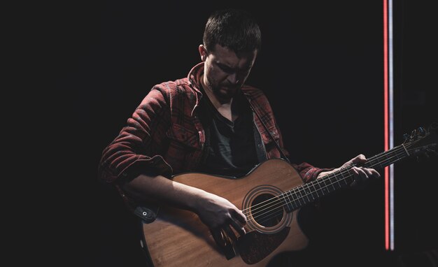 Male guitarist playing acoustic guitar in dark room.