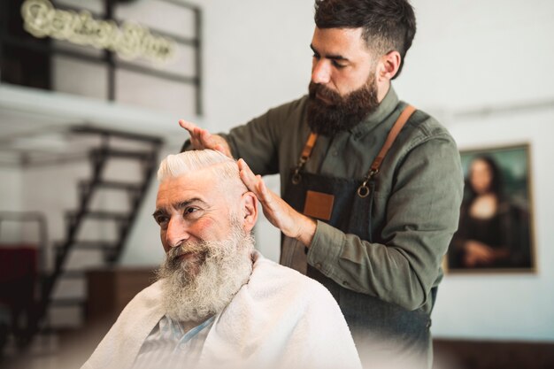 Male hairdresser working with hair of aged client