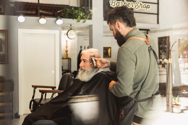 Male hairdresser working with hair of elderly client