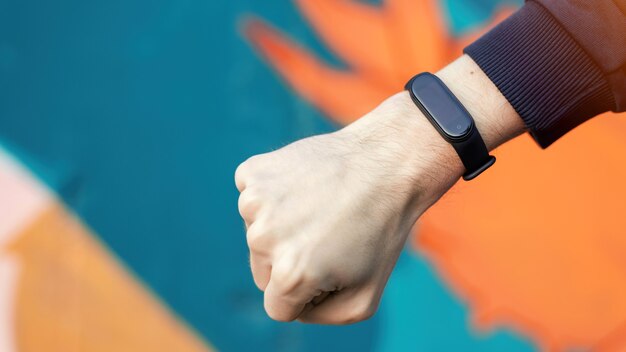 A male hand clenched into a fist with fitness bracelet on it, multicolored background