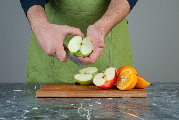Мужская рука резки зеленого яблока на мраморном столе.