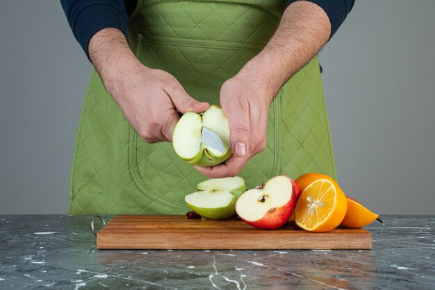 Male hand cutting green apple on top of wooden board on table.