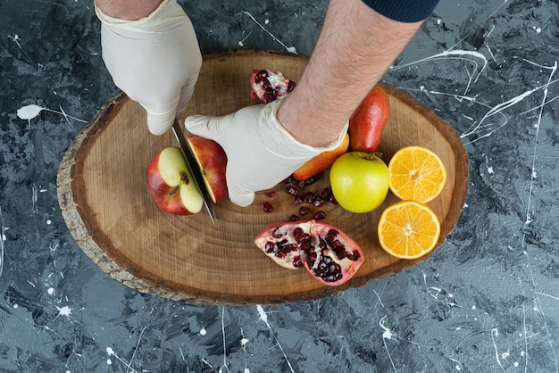 Free photo male hand cutting red apple on top of wooden board on table.